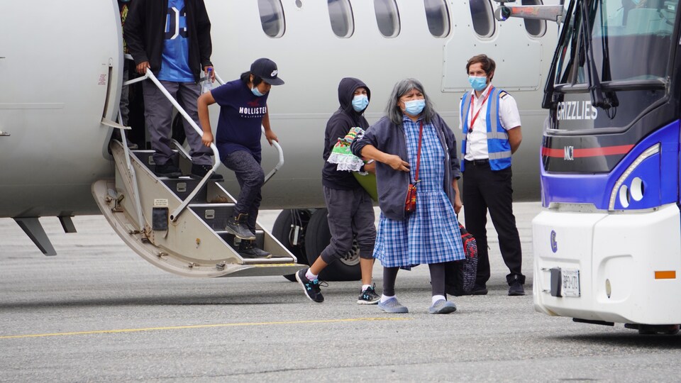 Quelques personnes descendent d'un avion militaire sur le tarmac pour se diriger vers un autobus.