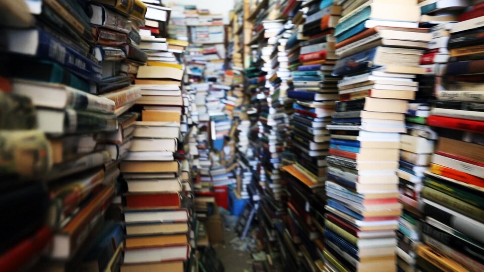 Des piles de livres s'accumulent dans une pièce étroite.