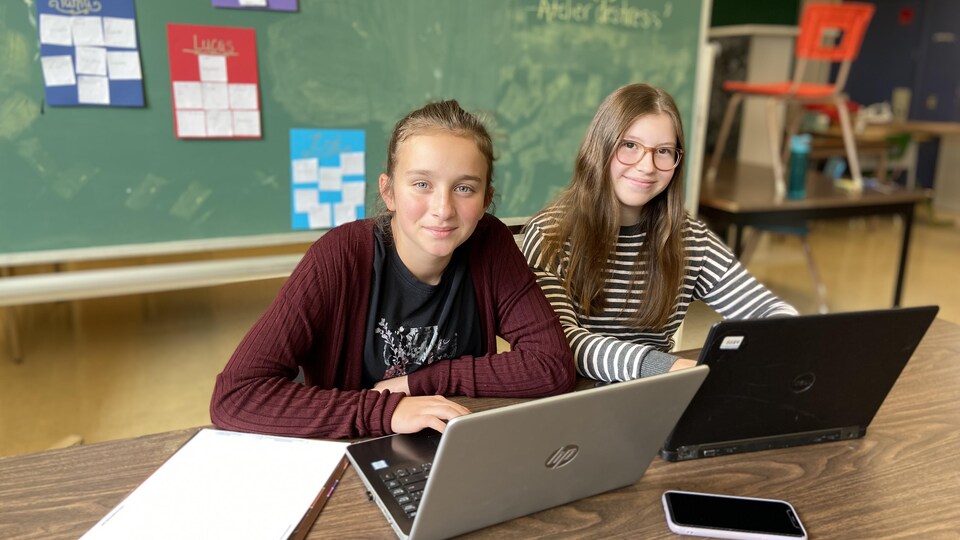 Ellia St-Pierre et Zoé Demers sont assises en classe devant des ordinateurs portables.