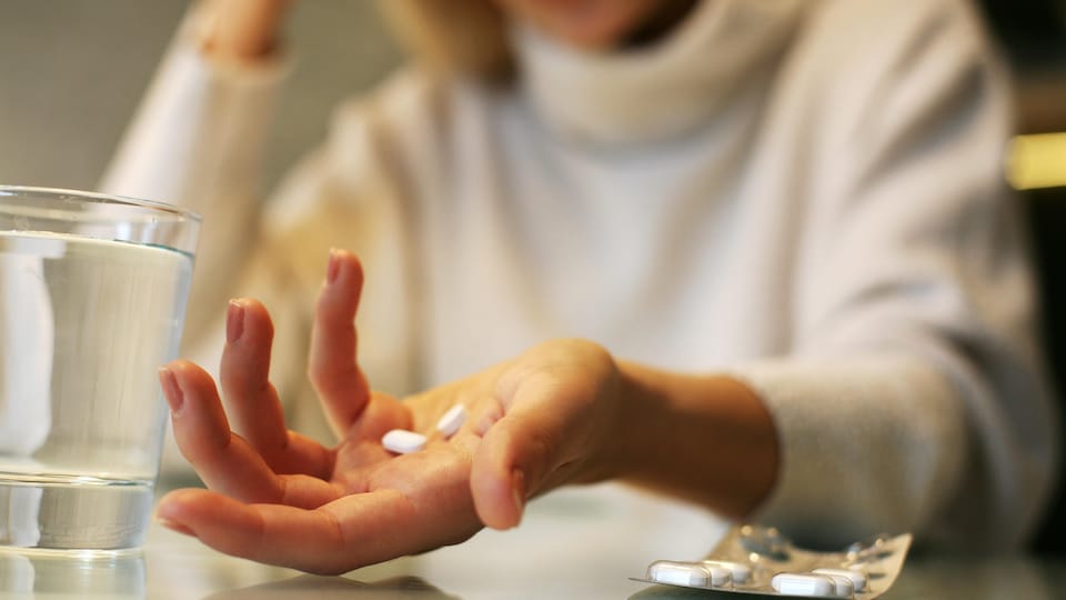 Une femme tient des cachets dans sa main.