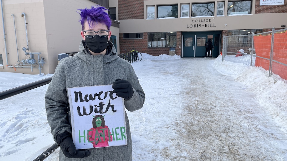 Une personne aux cheveux mauves montrant une affiche sur laquelle il est écrit Never with Heather.