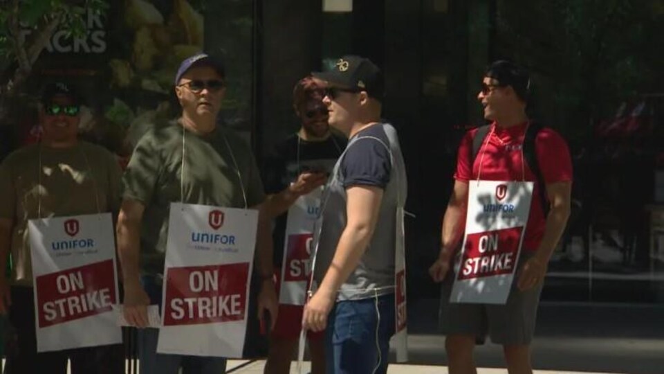 Des travailleurs en grève avec des pancartes accrochées au cou le 17 juin 2022 à Winnipeg.