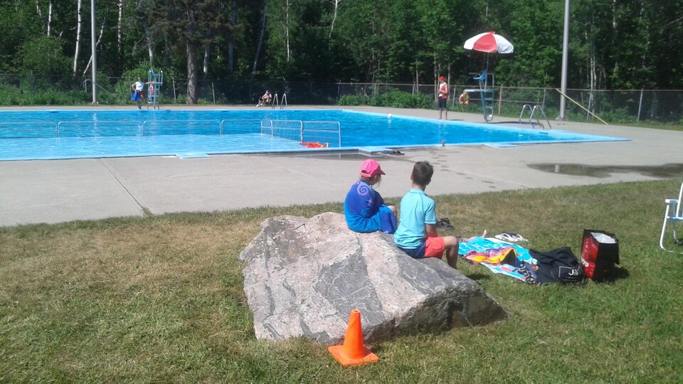Des enfants assis sur une roche regardent la piscine.