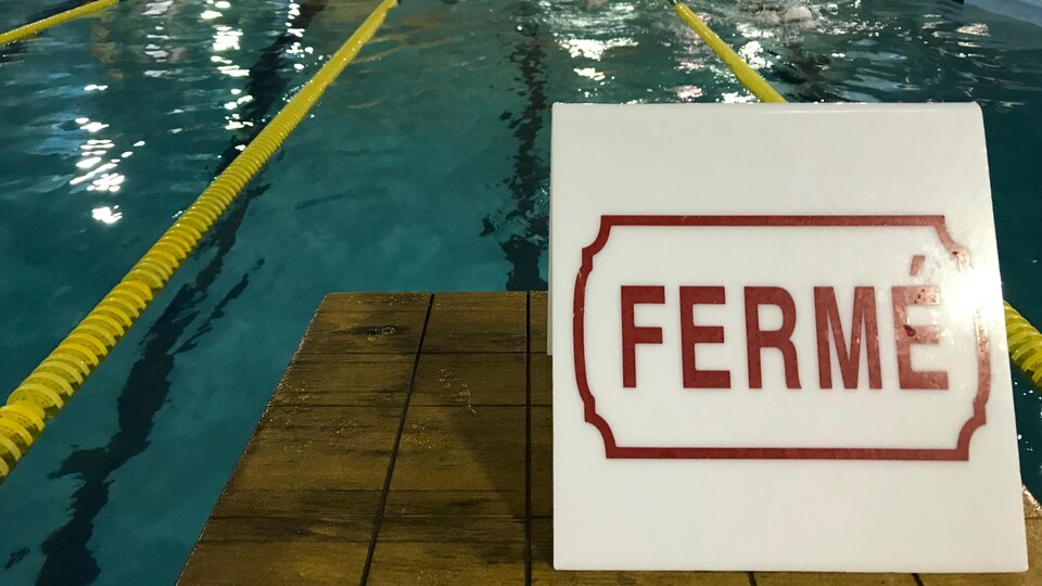 Vue sur les corridors d'une piscine intérieure avec une affiche où il y est inscrit « fermé » en rouge.
