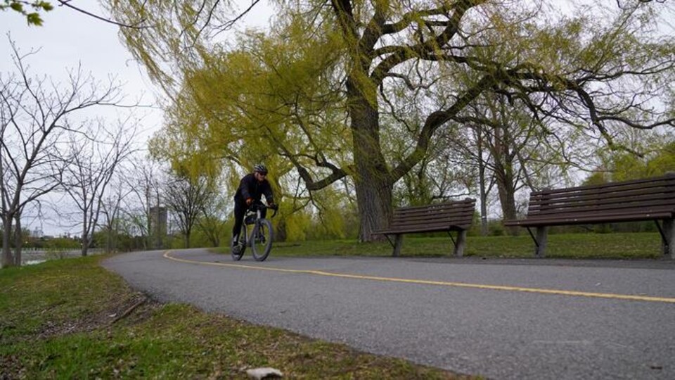 Un homme fait du vélo sur une piste cyclable en bordure d'un cours d'eau.