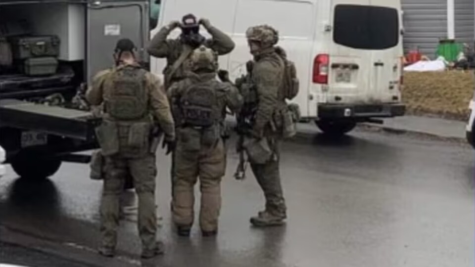 Quatre policiers vêtus d'uniformes d'allure militaire et équipés de fusils d'assaut ajustent leur équipement d'intervention.