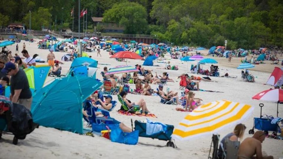 Des personnes sur une plage, dont certaines sont installées sous des tentes.