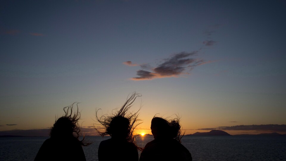 Les silhouettes de trois femmes qui regardent le coucher du soleil sur le traversier en Colombie-Britannique.
