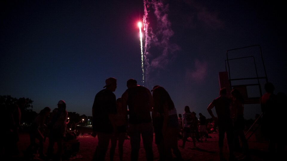 Des personnes rassemblées sur une plage la nuit avec des feux d'artifice dans le ciel.