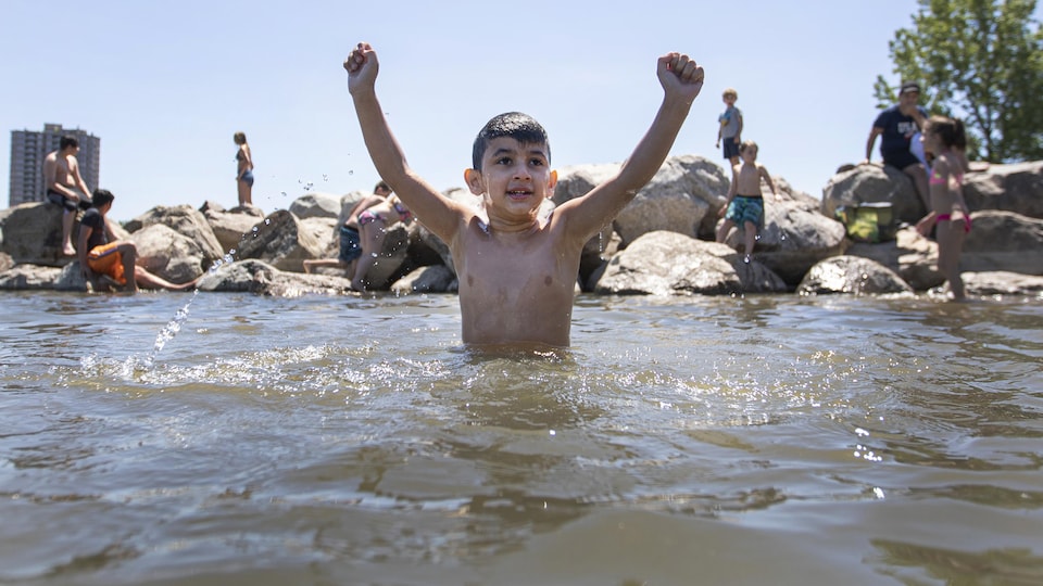 Un jeune garçon, dans l'eau jusqu'à la taille, avec les bras en l'air.
