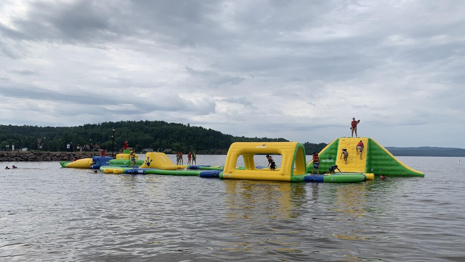 Une dizaine de jeunes circulent sur le jeu gonflable qui flotte sur l'eau. Une sauveteuse veille à leur sécurité.