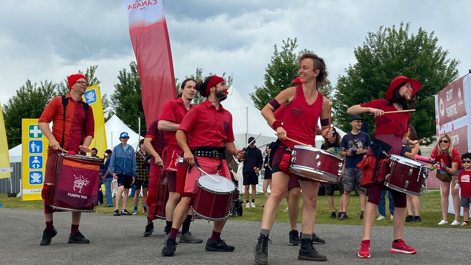 Un groupe de musiciens, vêtus de rouge, tapent sur des tambours devant des spectateurs.