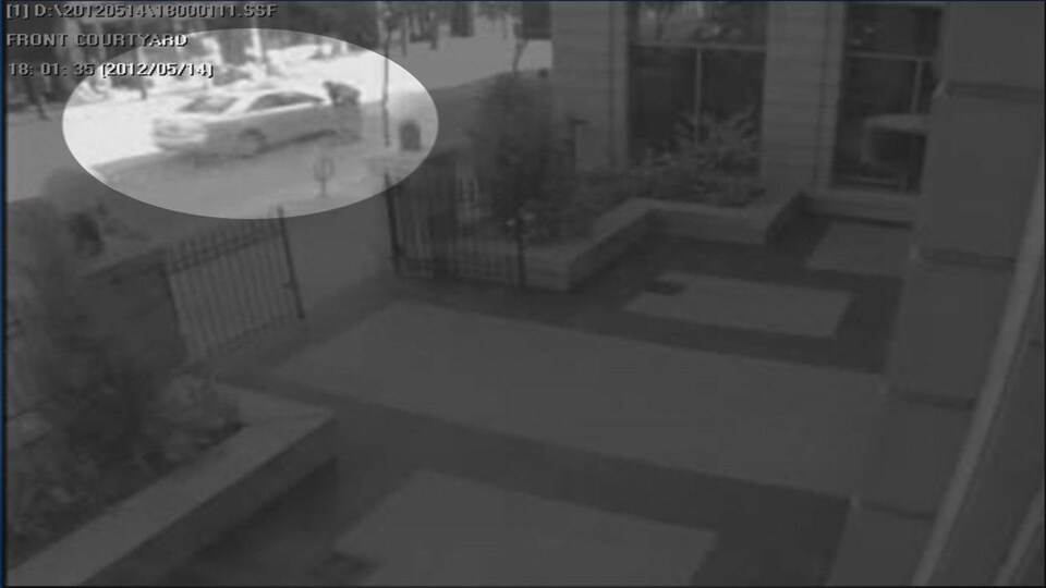 Capture d'écran d'une caméra de surveillance sur laquelle on voit une voiture et un homme proche du véhicule. 
