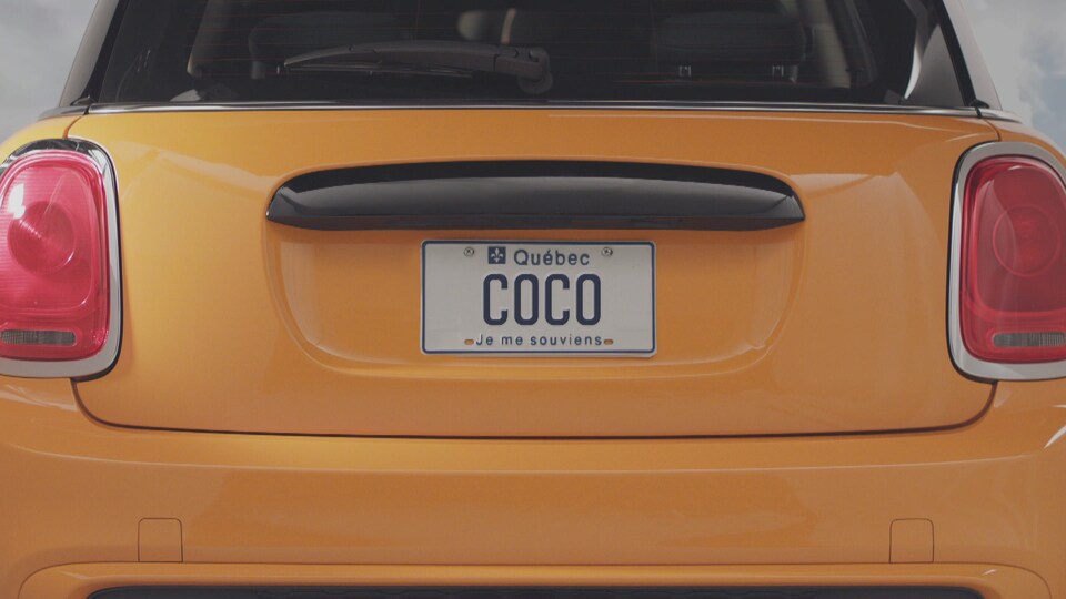 Exemple d’une plaque personnalisée qui serait conforme. La plaque porte l’inscription « COCO ». Elle est installée à l’arrière d’une voiture à hayon de couleur jaune.