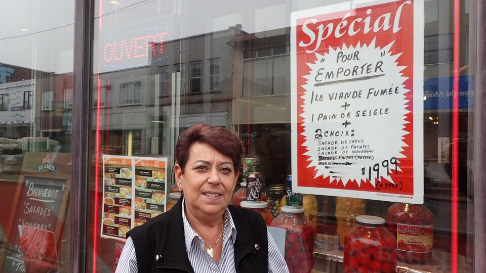Une femme debout devant la vitrine d'un restaurant dans laquelle on voit des pots de piments et une affiche.