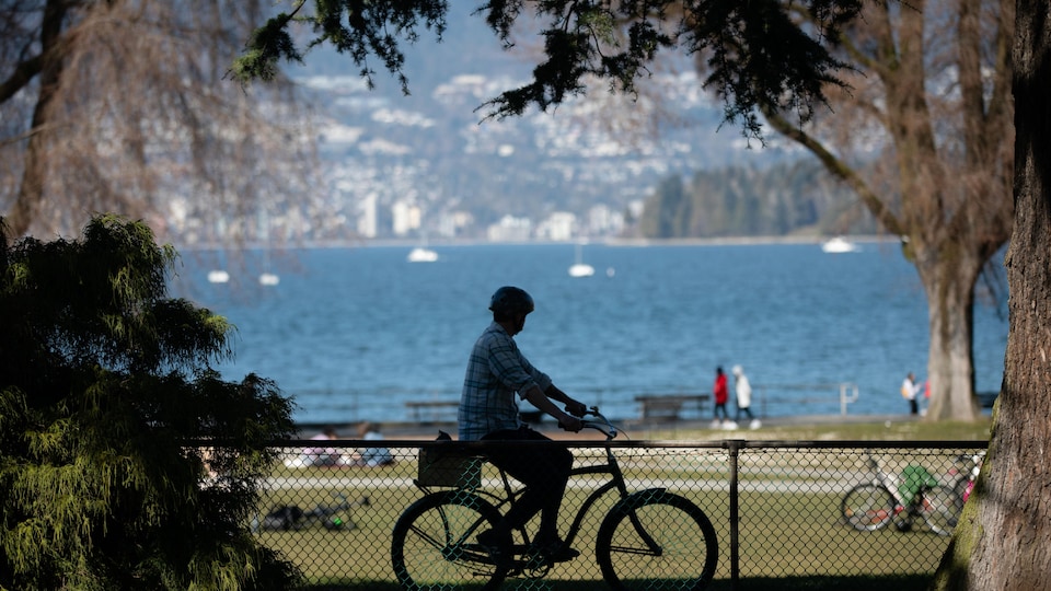 Un homme fait du vélo devant la plage de Kitsilano à Vancouver.