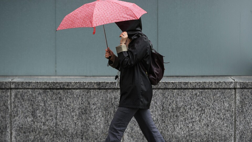 Une personne se protège de la pluie à l'aide d'un parapluie et d'un imperméable en marchant sur la rue Elgin, à Ottawa, le mardi 17 mai 2022 (archives).