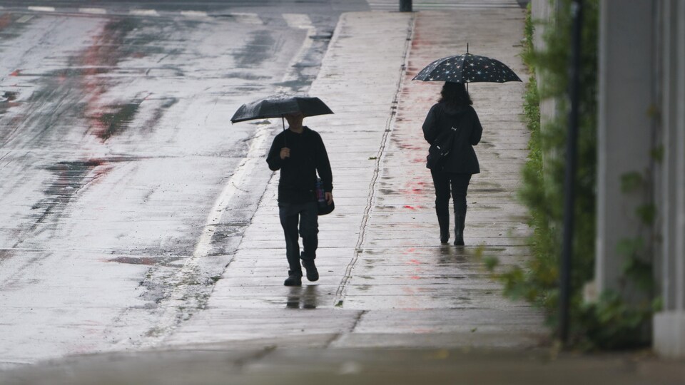 Deux personnes marchent sur un trottoir et tiennent un parapluie.