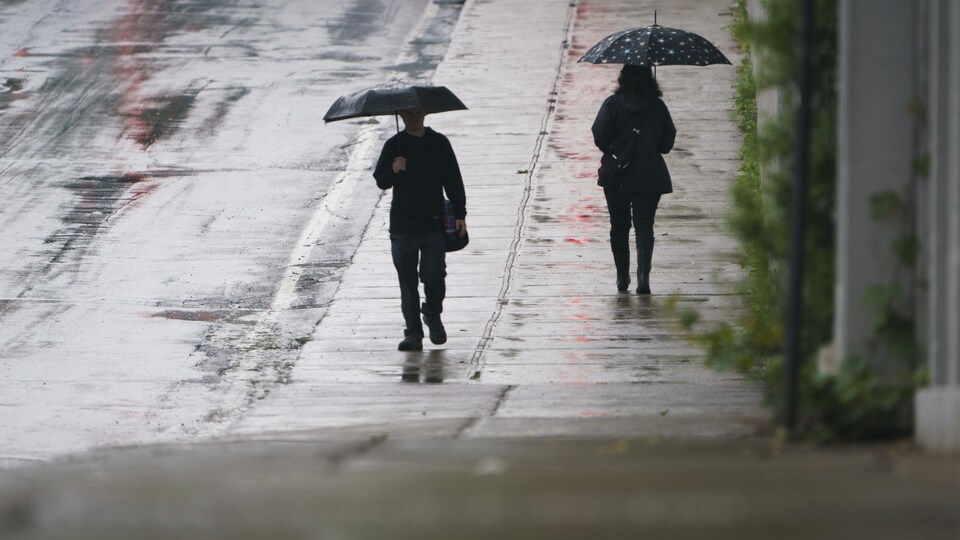 Un homme une femme marchent en direction opposée, chacun sous un parapluie.