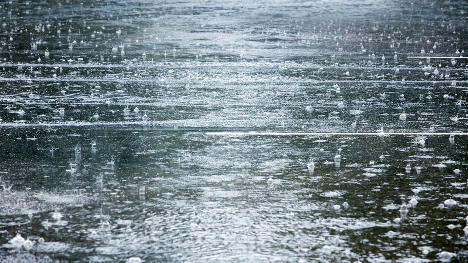 Une photo d'une route inondée par la pluie. De nombreuses gouttes tombent du ciel.