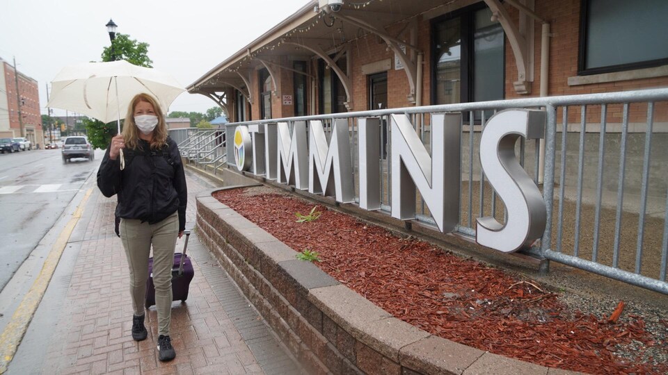 Une femme marche dans une rue de Timmins avec un parapluie. Elle porte un masque.