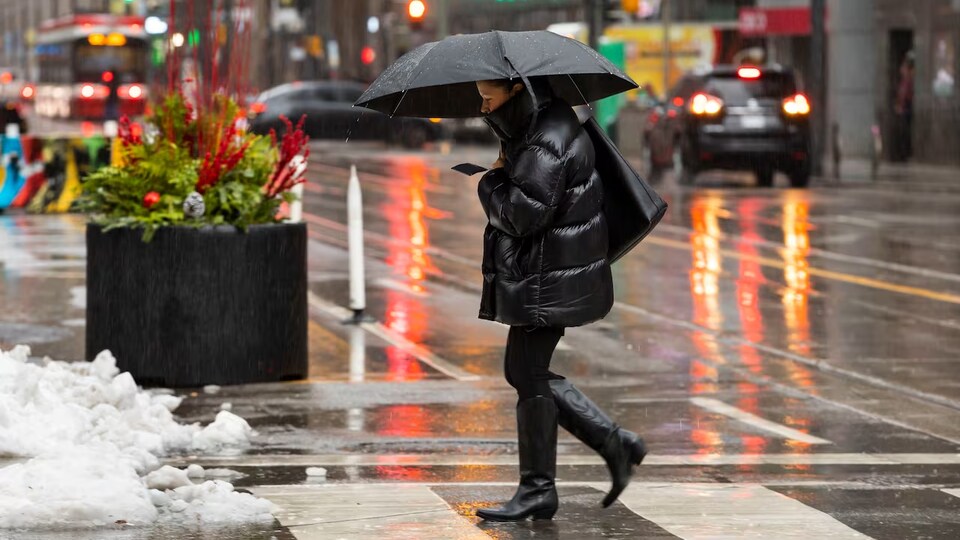 Une femme traverse une rue sous la pluie en hiver.