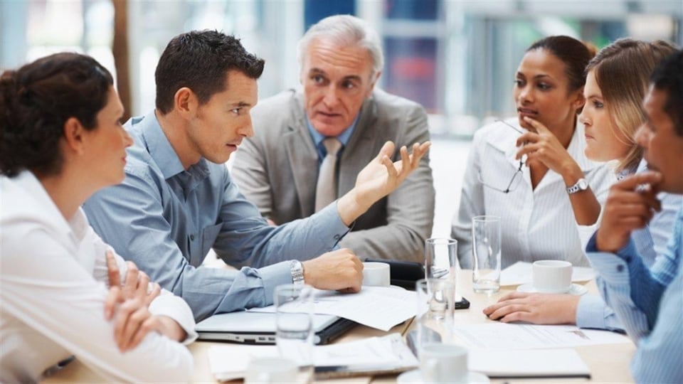 Six personnes sont assises autour d'une table et discutent.