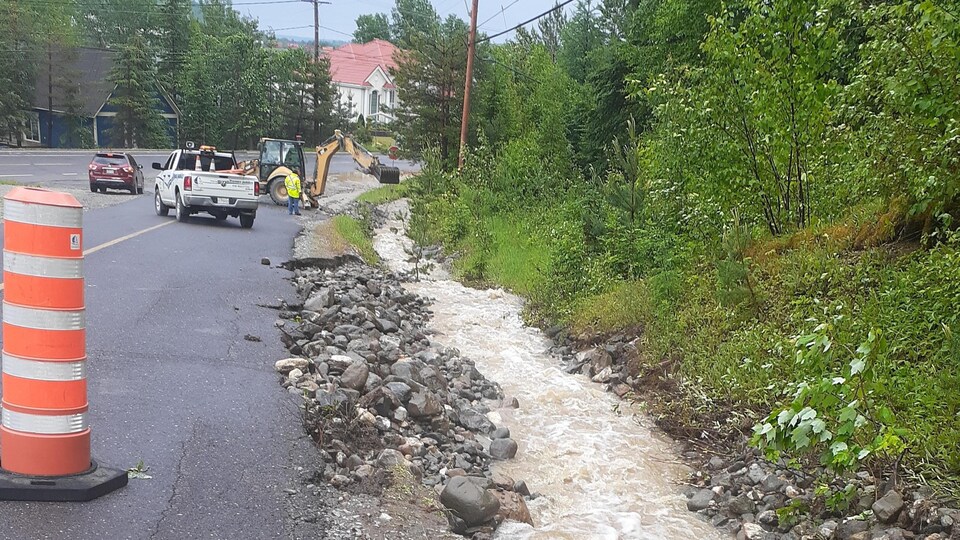 L'eau coule avec un fort débit dans un fossé. Des travailleurs creusent pour atténuer les effets de l'inondation.