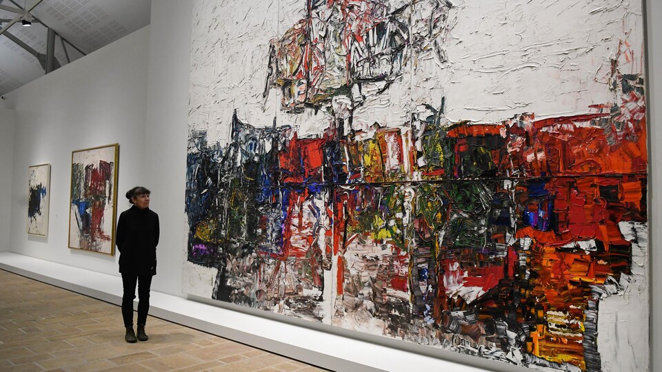 Une femme se tient devant une peinture gigantesque dans une salle d'exposition. 