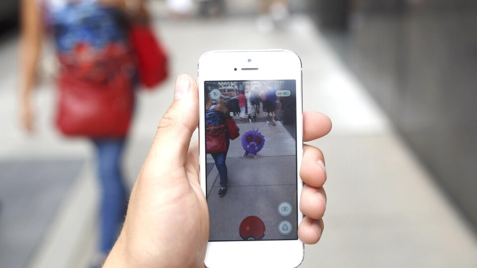 Un pokémon apparaît sur le téléphone d'un joueur de Pokémon Go dans une rue de Toronto.