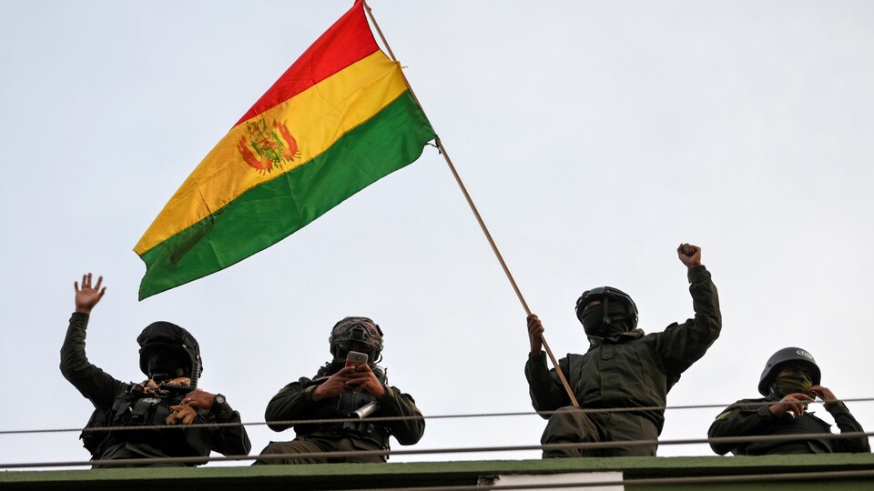 Des policiers masqués portent un drapeau bolivien.