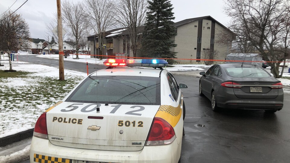 Une voiture de la Sûreté du Québec et une voiture noire près d'un ruban rouge.