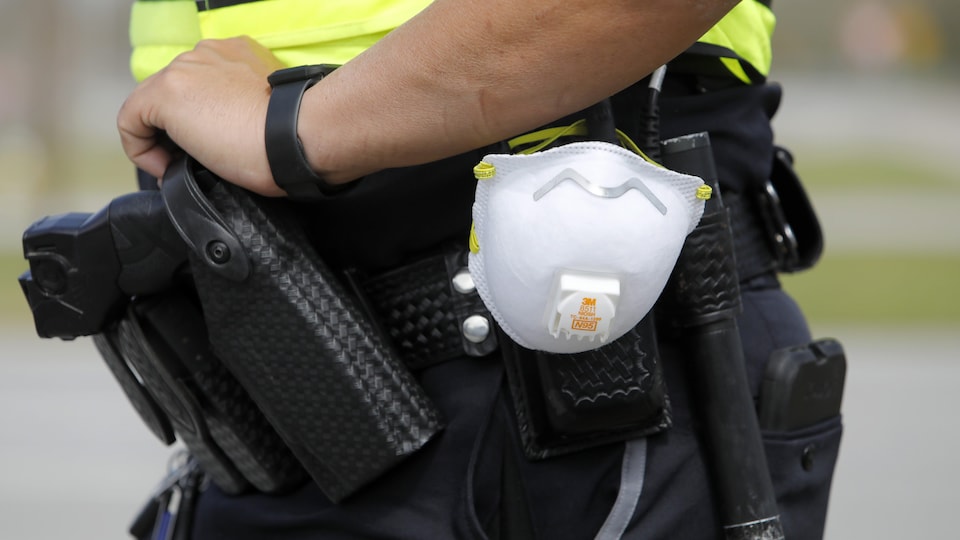 Un masque de protection est accroché à la ceinture d'un policier, à côté de son arme de service.