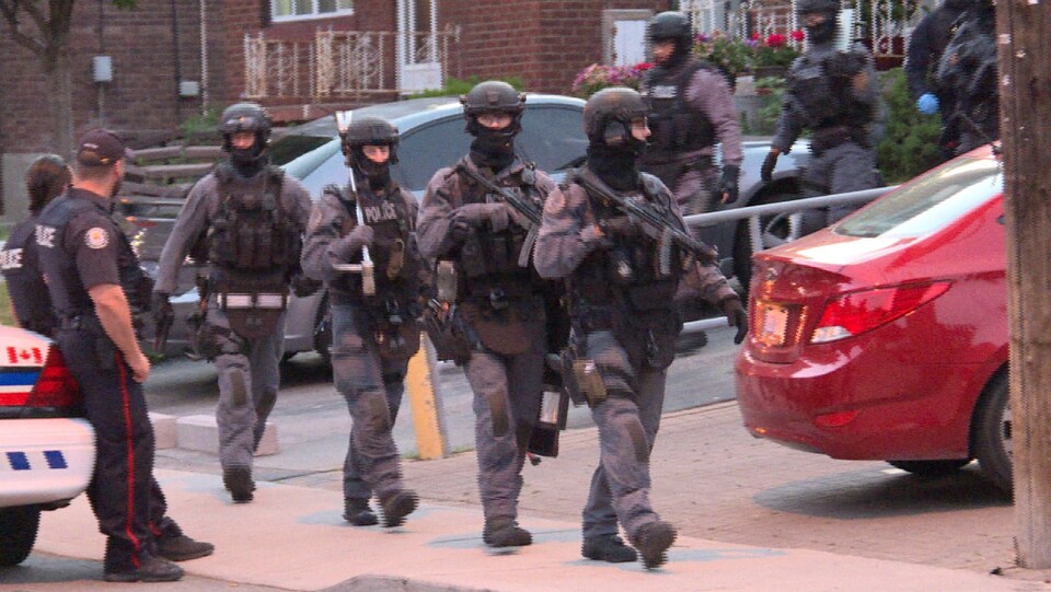 Photo d'agents de l'escouade tactique habillés en gris qui sortent d'un domicile.
