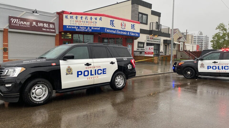 Deux véhicules de police sont stationnés devant des commerces dans le quartier chinois. Un ruban jaune barre le passage.