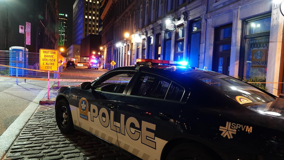 Une voiture de police est garée devant un périmètre de sécurité.