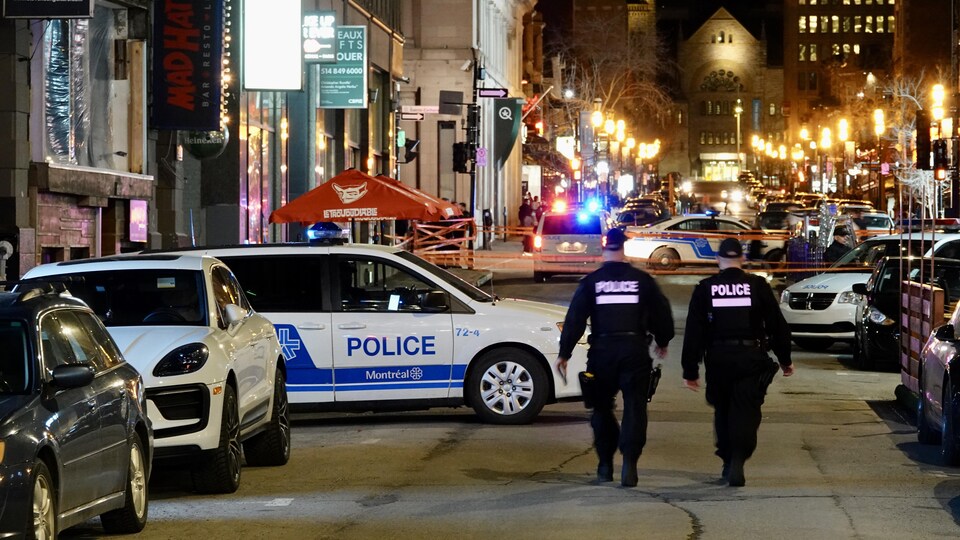Deux policiers marchent dans la rue près d'un périmètre de sécurité. 