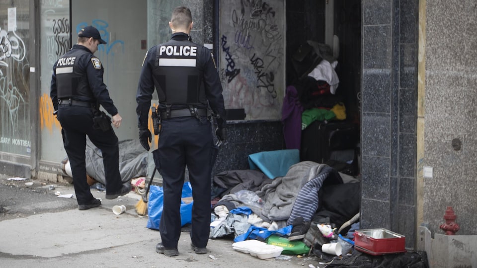 Des policiers près d'une entrée de logement devant laquelle on voit plein de détritus et de vêtements qui jonchent le sol.