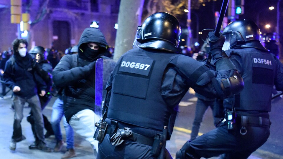 Un manifestant masqué donne un coup de pied aux policiers, qui eux ont leur bâton levé.