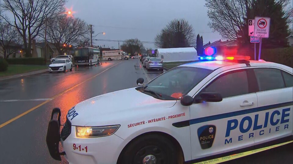 Des véhicules de la police sont stationnés dans une rue d'un quartier résidentiel.
