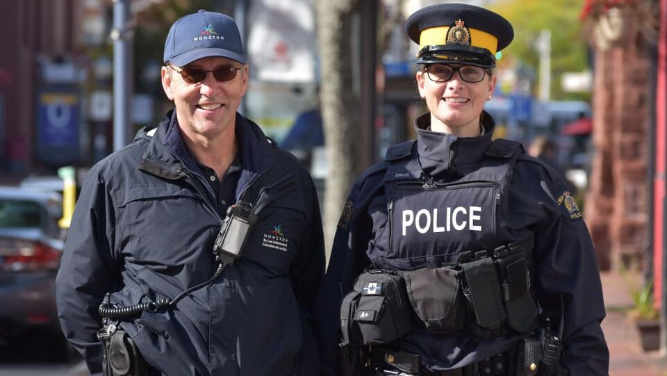 Un homme et une femme en uniforme côte à côte sur un trottoir.