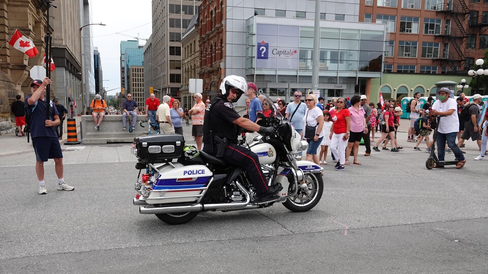 Un agent à moto regarde vers la caméra, devant une petite foule.