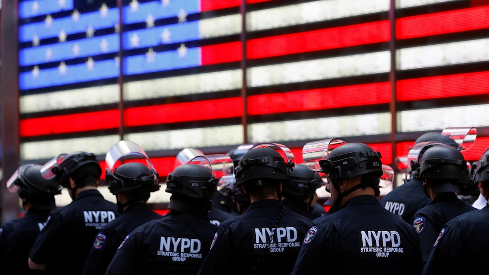 Une douzaine d'agents portant des casques sont rassemblés devant un drapeau lumineux des États-Unis.