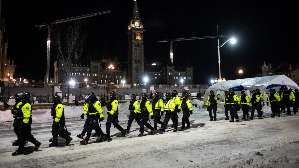 Des policiers marchent en rangs serrés dans la rue, de nuit, en hiver.