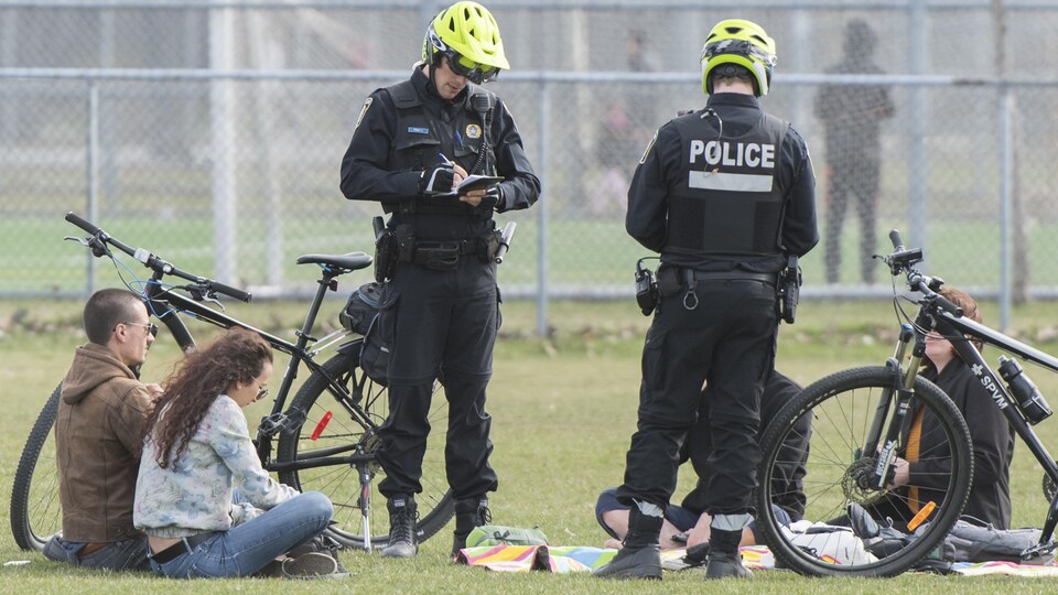 Deux policiers dressent des contraventions alors que des gens sont assis par terre.