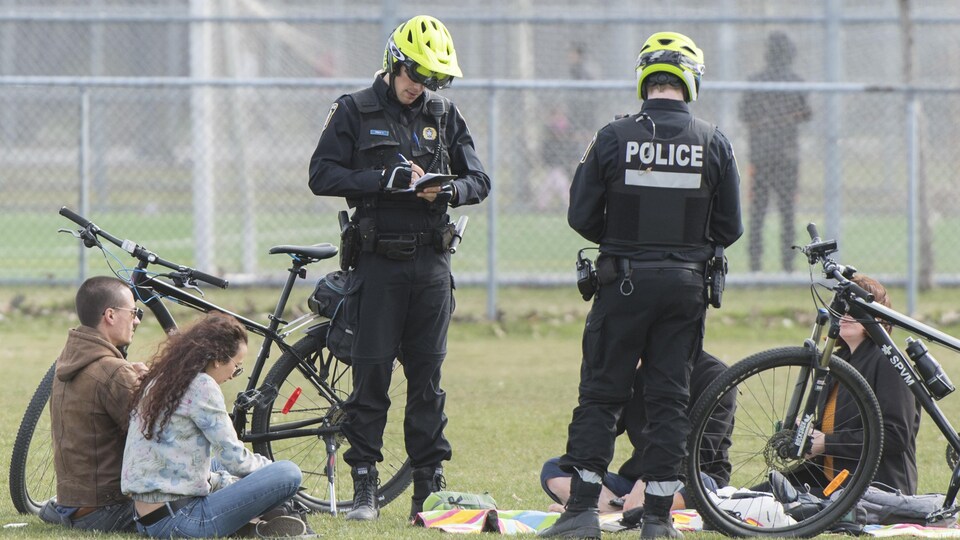 Deux policiers écrivent des contraventions alors que des gens sont assis par terre.