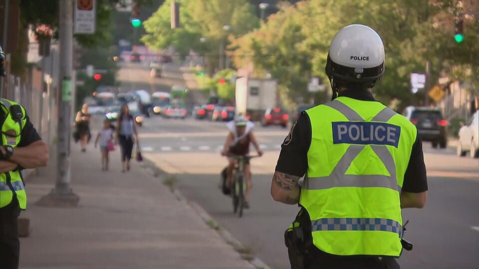 Un policier de dos portant un dossard au bord d'une rue de Québec.