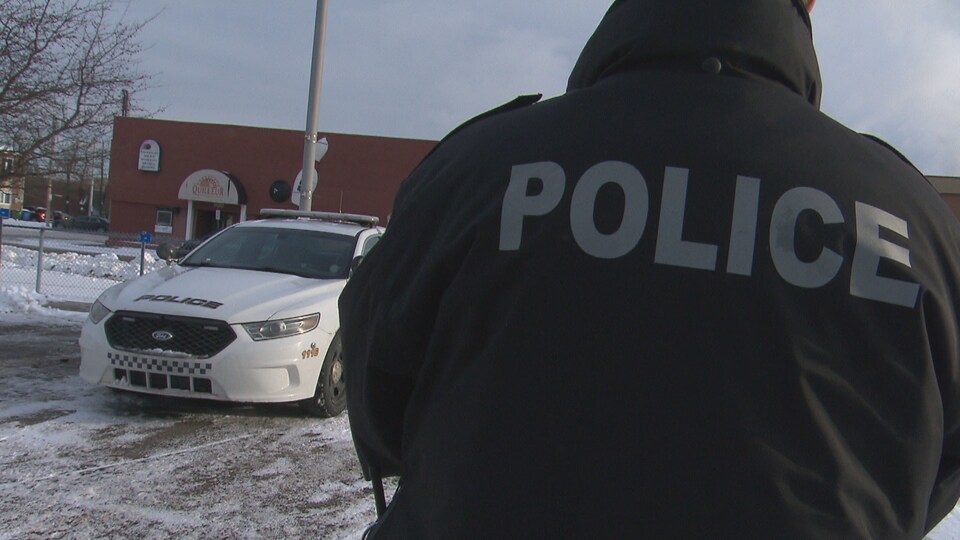 Un policier de dos devant sa voiture.