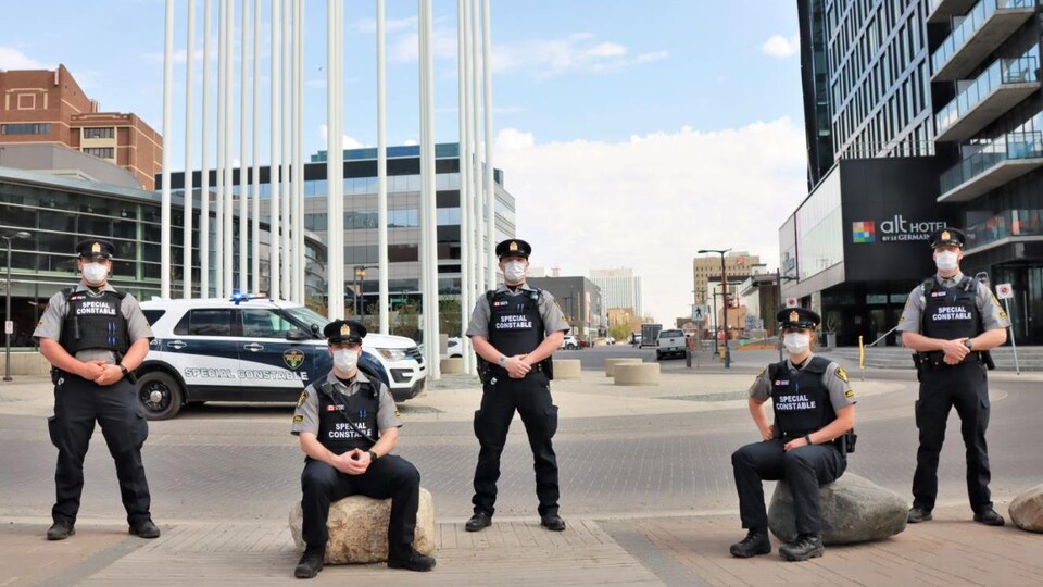 Cinq agents du Service de police de Saskatoon près d'un de leur véhicule.