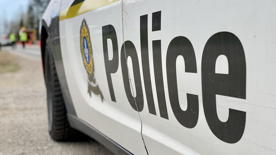 Une voiture de police de la Sûreté du Québec avec des agents au loin.